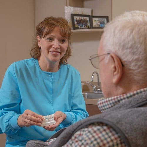 Dental team member showing dental patient a model with dental restoration