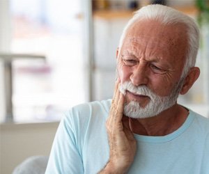 Ia man touching his cheek due to failed dental implants