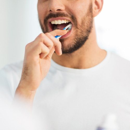 Bearded man brushing his teeth in the bathroom mirror
