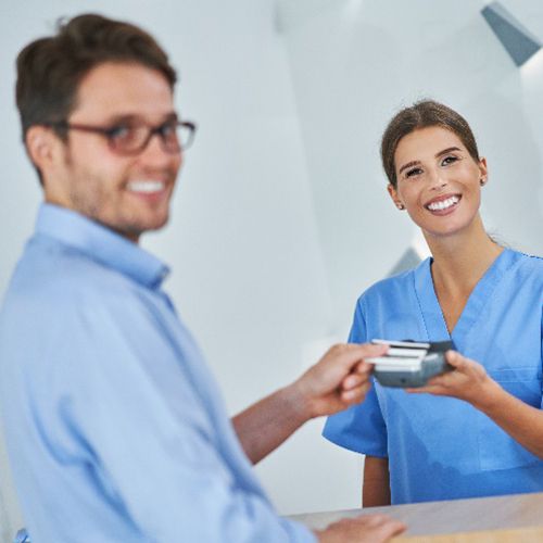 Dental receptionist and patient smiling while paying for treatment