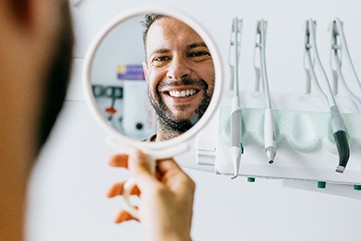 Man smiling while looking at reflection in dentist's mirror