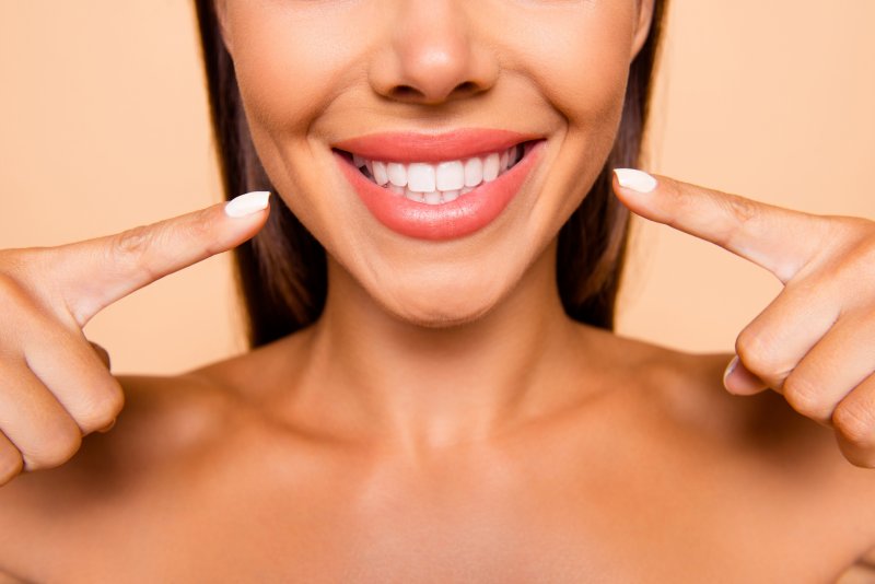 an up-close view of a woman pointing to her new smile that contains veneers