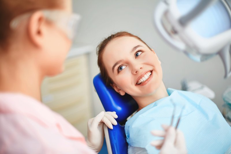 Woman laying in dental chair smiling up at dentist